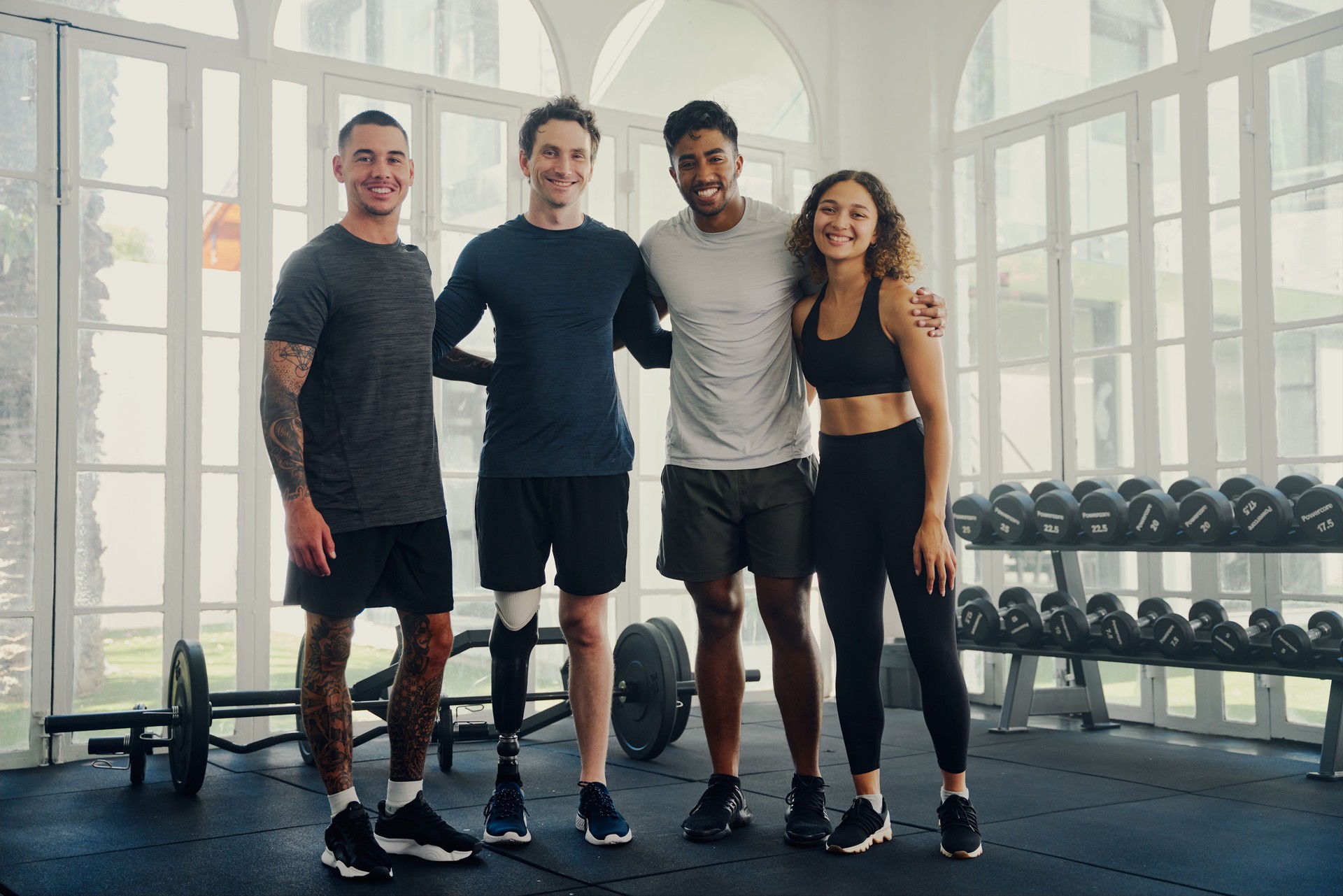 Group portrait of happy multiracial young adults in sportswear looking at camera at the gym